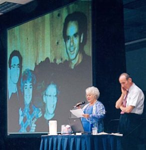 Judith Whitson and Kenneth Wapnick at conference (projected photo of Ken, Judy, Helen and Bill behind them) at Miracle Distribution Center conference